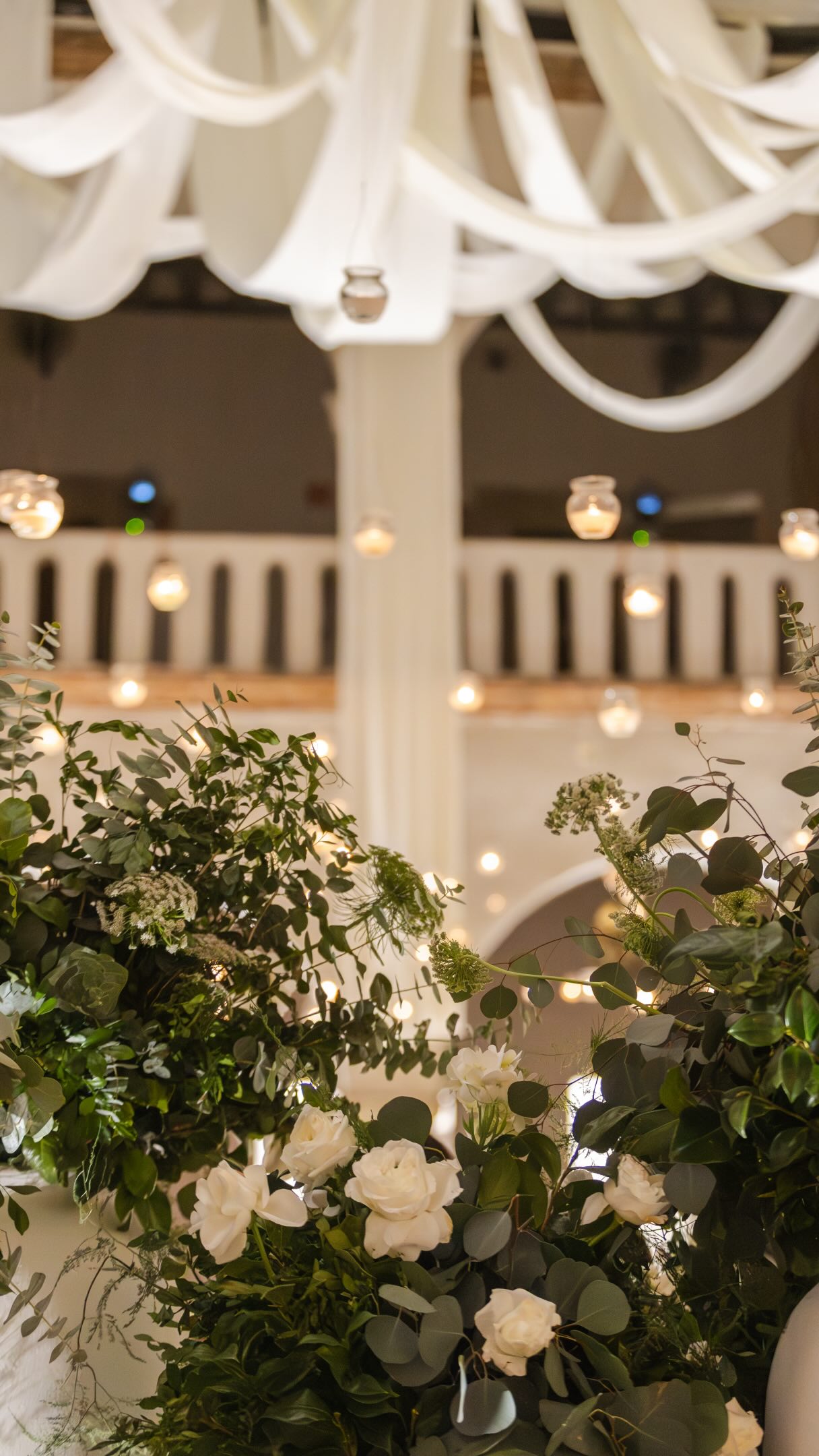 Arreglo floral blanco y verde con guirnaldas de luces bajo telas drapeadas